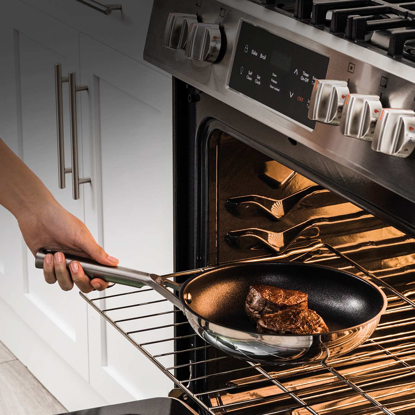 Hand placing a stainless steel Ninja frying pan with steak into an oven